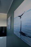 A wall with two framed artworks depicting a bird and a whale, with a window to the left.