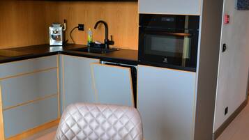 Cocina compacta con horno integrado, lavamanos y encimera. Hay un comedor con mesa y sillas.