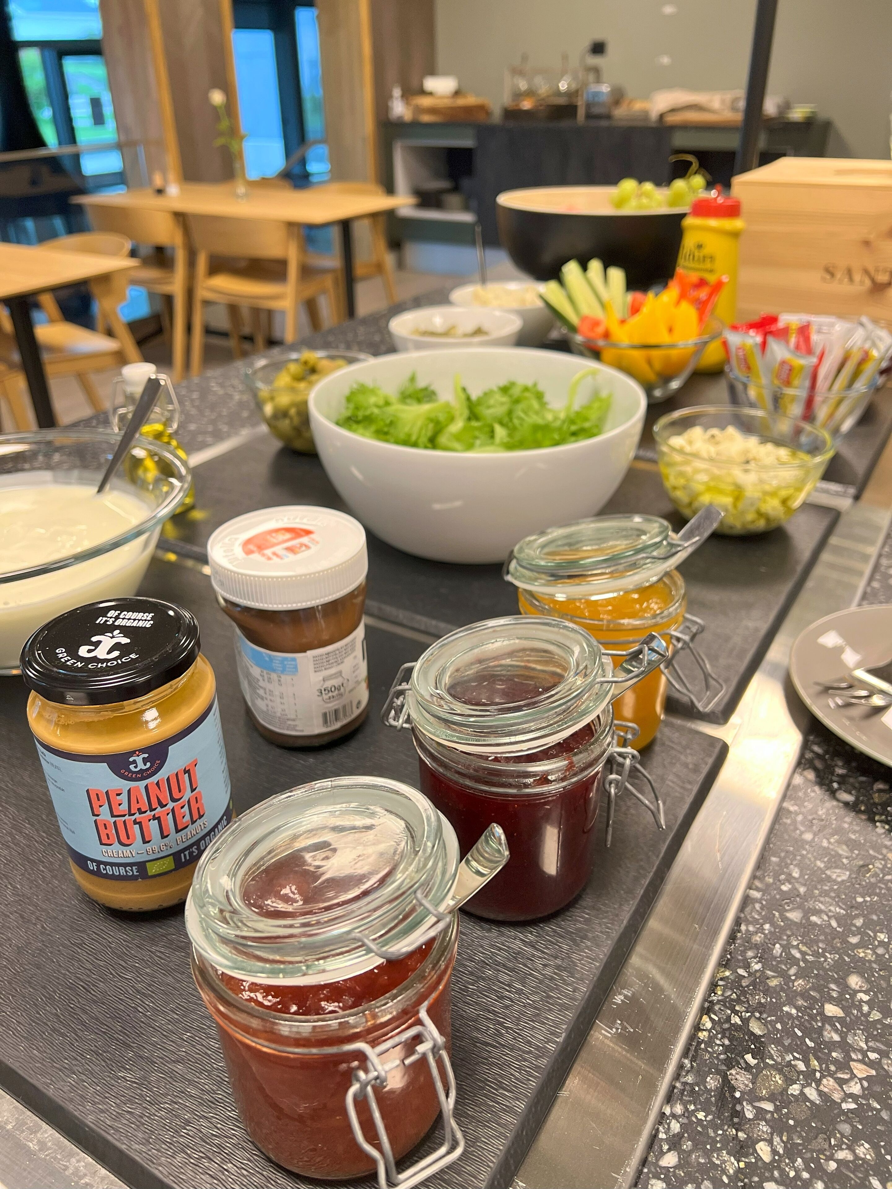 Un plan de travail de cuisine avec divers aliments, notamment des pots de beurre de cacahuète, de confiture et un saladier rempli de salade.