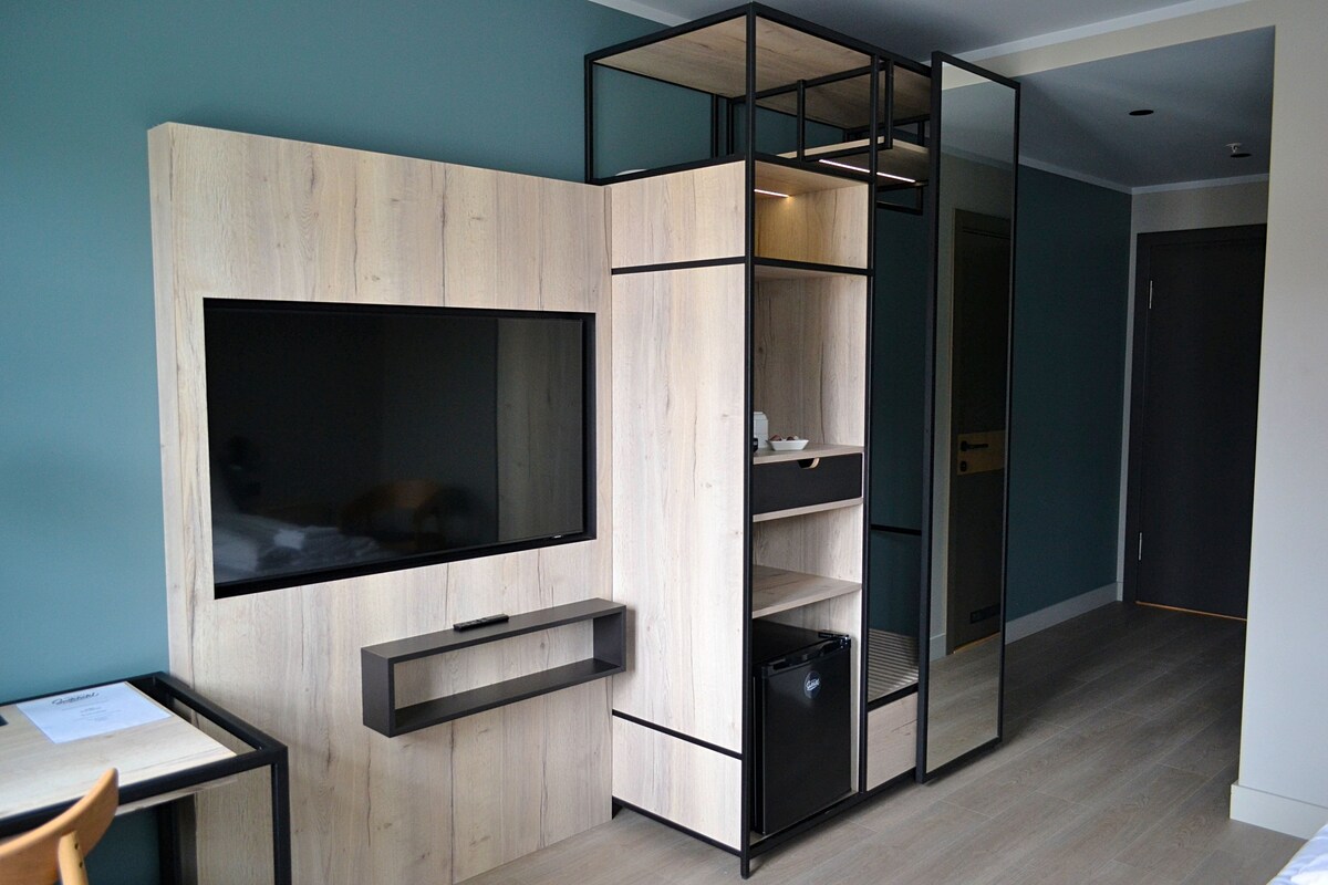 A modern room with a built-in TV, wooden shelving, and a compact refrigerator.