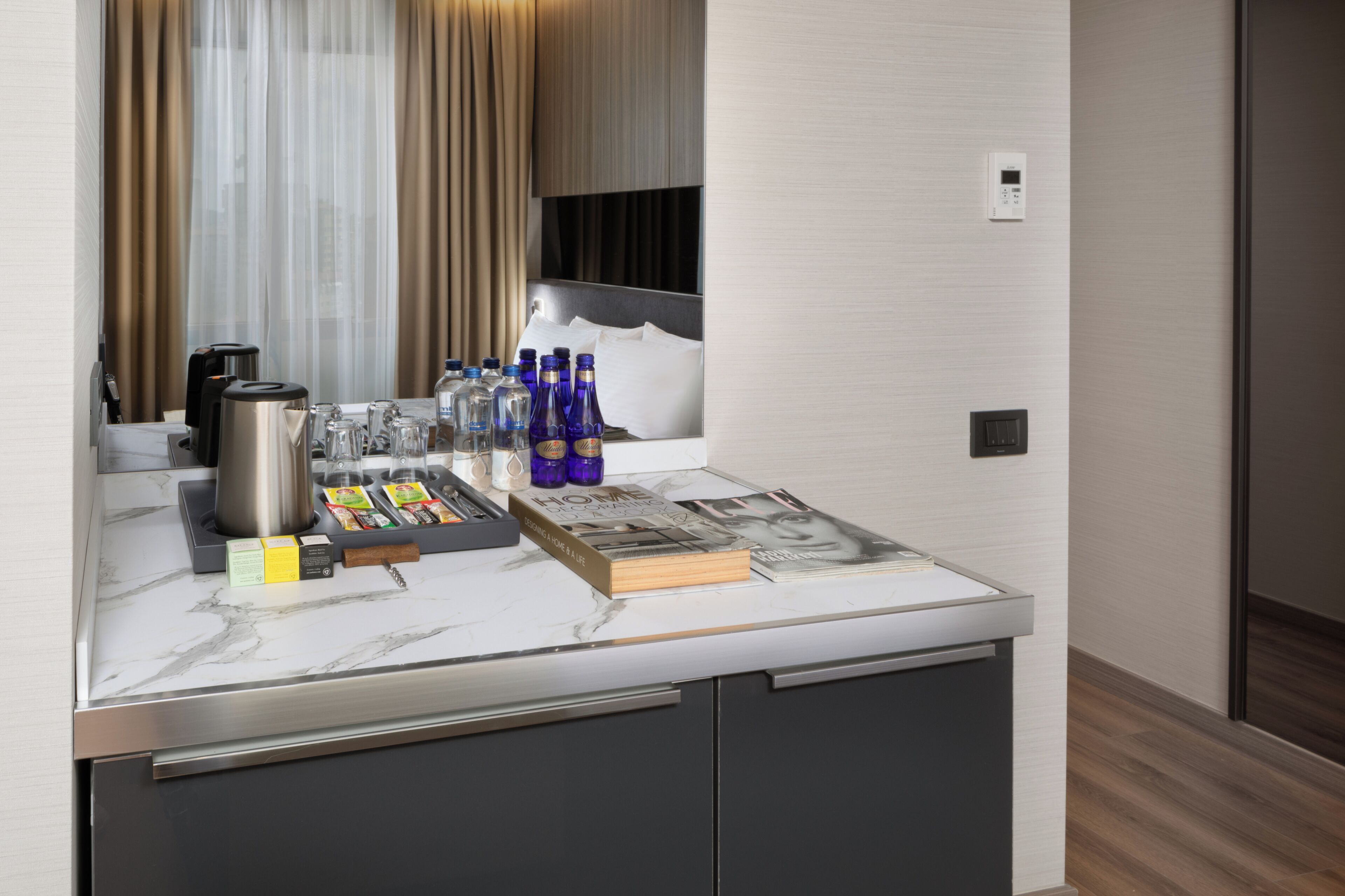 A modern hotel room with a marble countertop, a coffee machine, a mini-fridge, and a selection of bottled water and snacks.