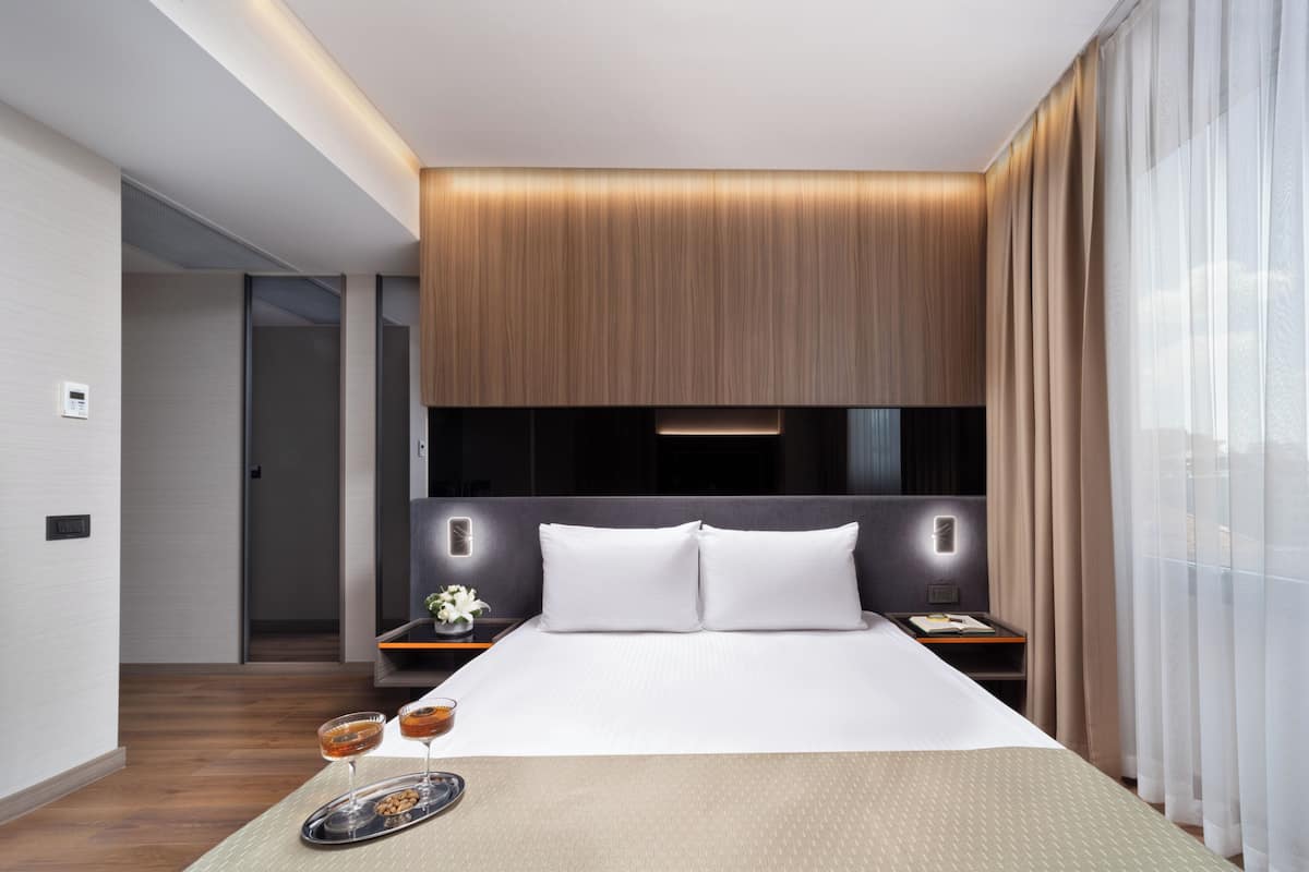 Una habitación de hotel moderna con una cama grande, mesitas de noche y un ventanal con cortinas.