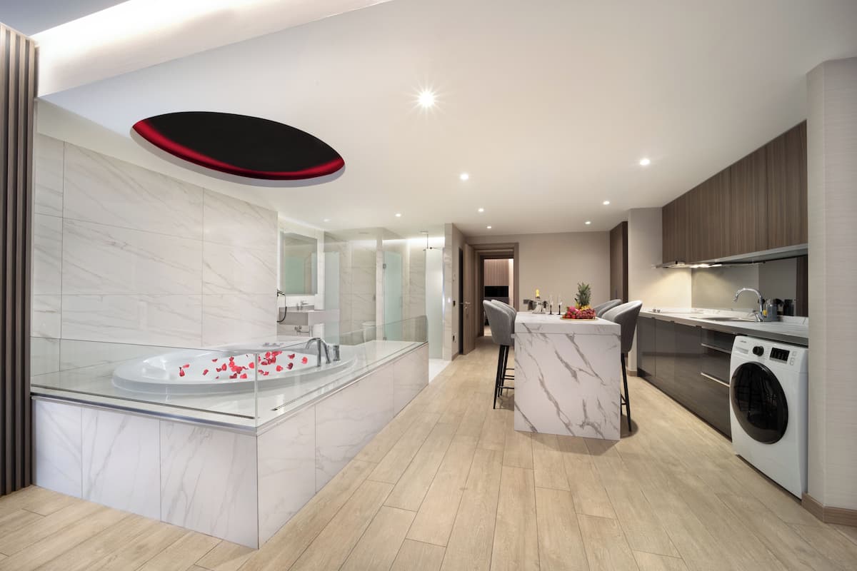 Una cocina moderna con una isla central, lavadora integrada y bañera de hidromasaje con mampara de vidrio.