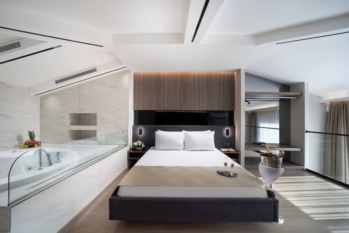 Habitación de hotel moderna con una cama grande, baño con paredes de vidrio y vista a la ciudad.