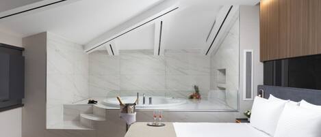 Ein modernes Schlafzimmer mit einem großen Bett, einem eingebauten Schreibtisch, einem Schminktisch mit Spiegel und einem separaten Badezimmer mit Badewanne und Dusche.