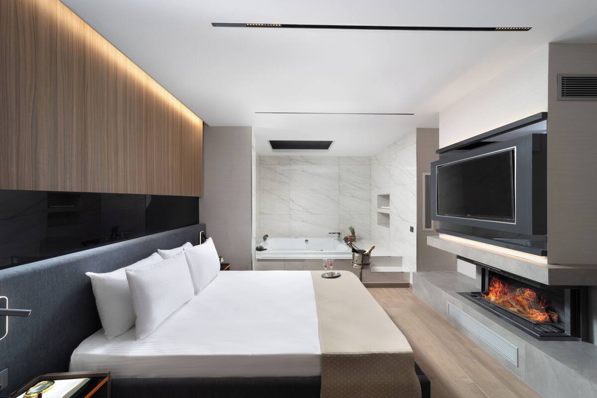 Un dormitorio moderno con una cama grande, un televisor montado en la pared y una chimenea.