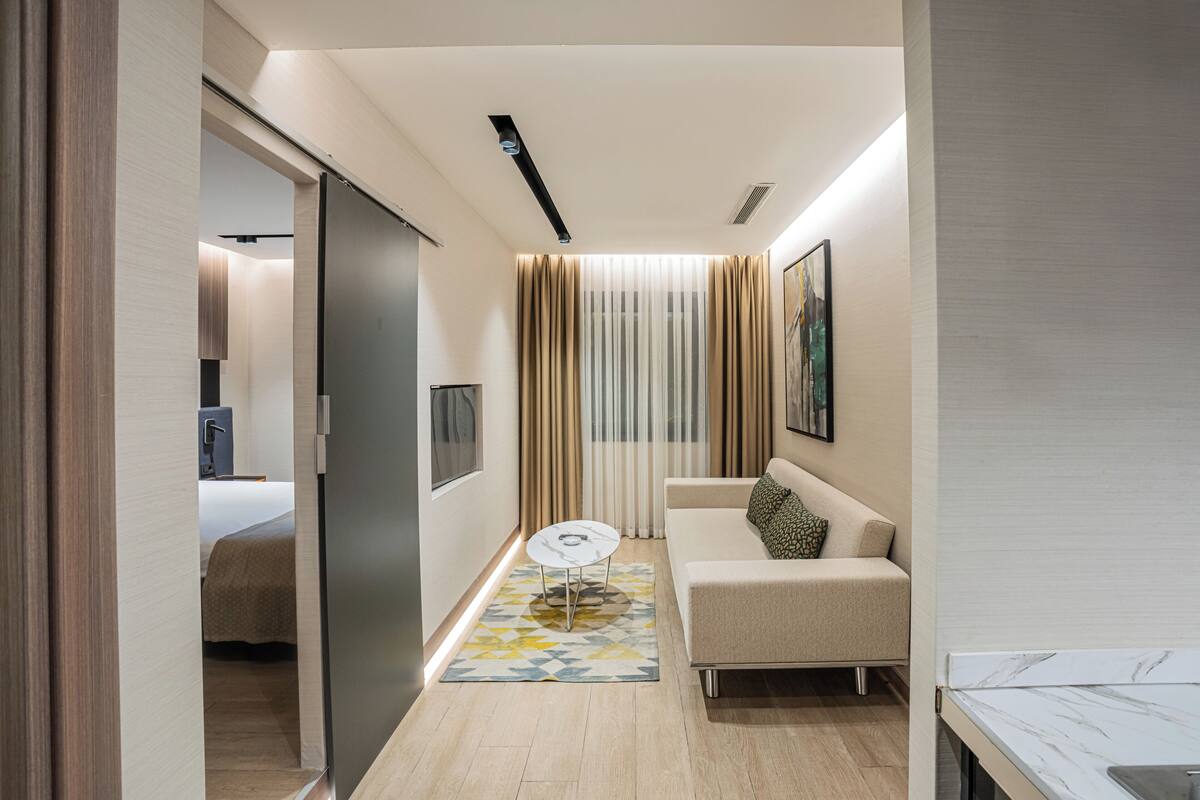 Una habitación de hotel moderna con sofá, una mesita redonda, cama y ventana con cortinas.