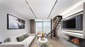 A modern living room with a sofa, coffee table, fireplace, TV, and staircase. - Nish Palace Besiktas (Istanbul)