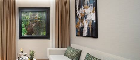 A modern living room with a sofa, a coffee table with fruit, and a large window with curtains.