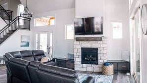 A modern living room with a fireplace, black leather sofa, and a staircase. - Unobstructed Lake Views! Bunk Room w/ Video Games! Ping Pong & Foosball! Extra Fridge & Freezer Space! (Fish Haven)