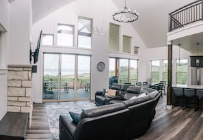 A spacious living area with a large black leather sofa, a stone fireplace, and a view of a patio with outdoor furniture.