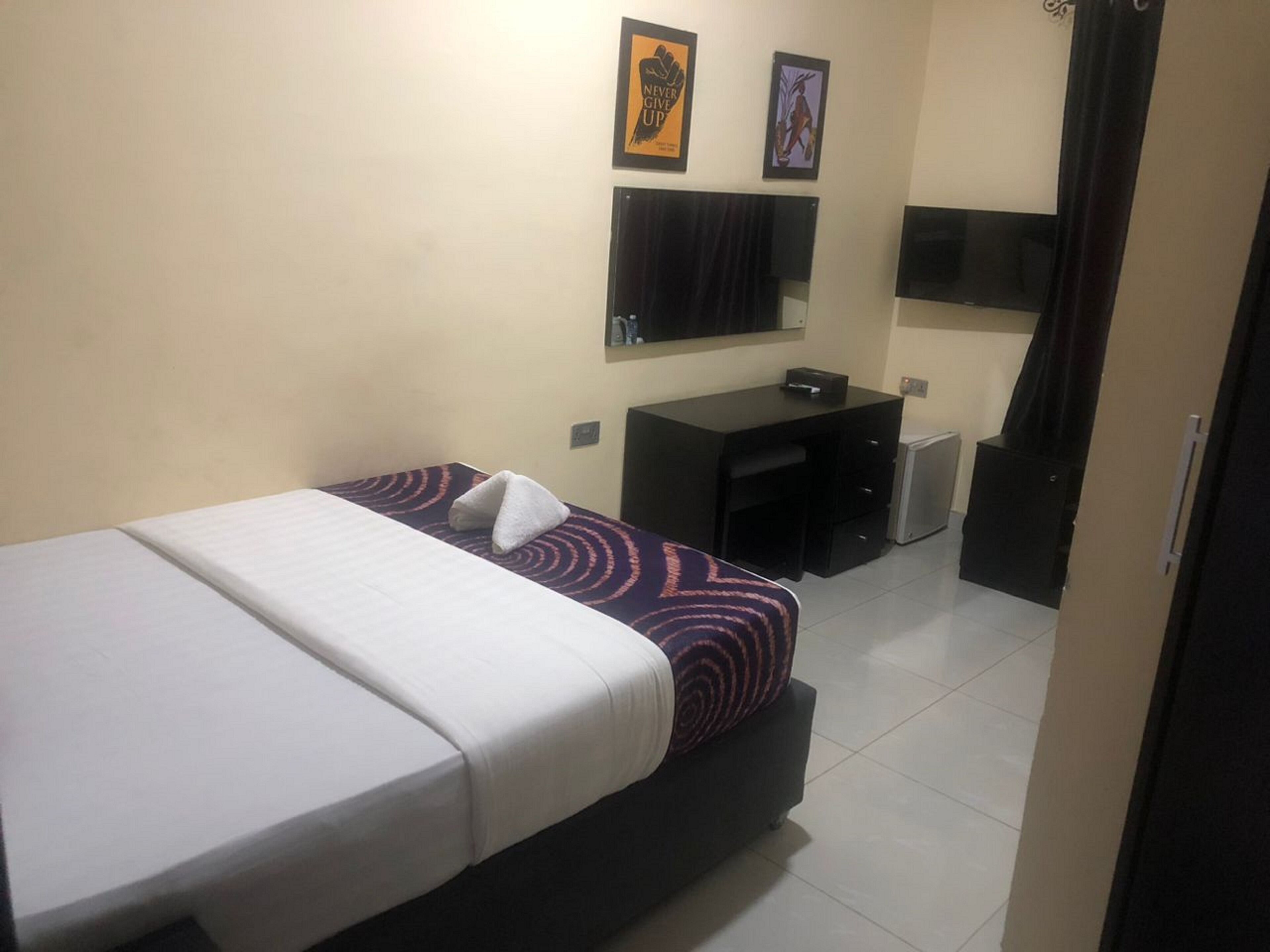 A hotel room with a bed, a desk, a chair, a small refrigerator, and a television on the wall.