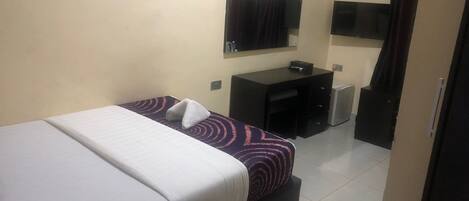 A hotel room with a bed, a desk, a chair, a small refrigerator, and a television on the wall.