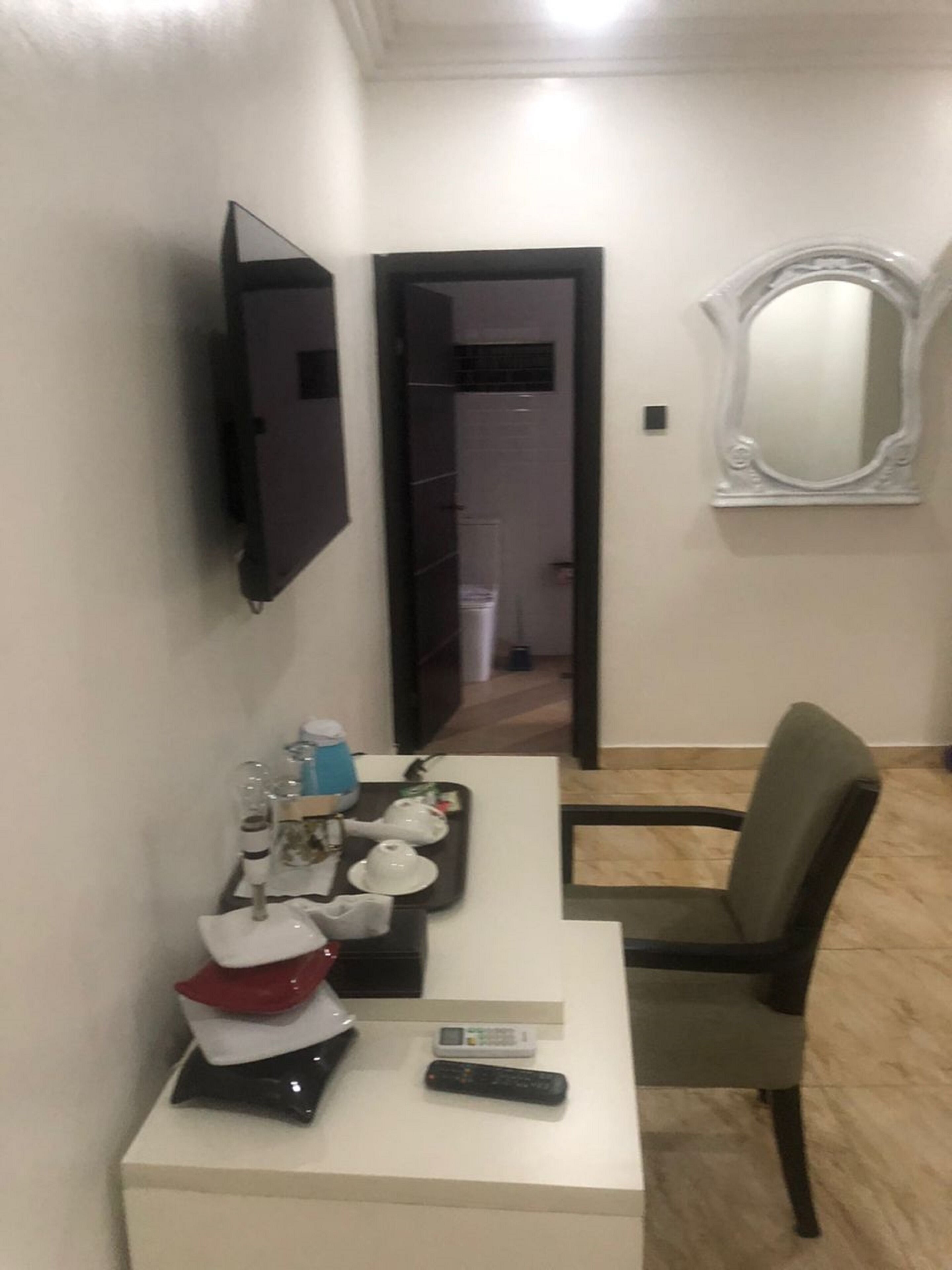 A small room with a white desk, a chair, a flat-screen TV mounted on the wall, and a mirror.