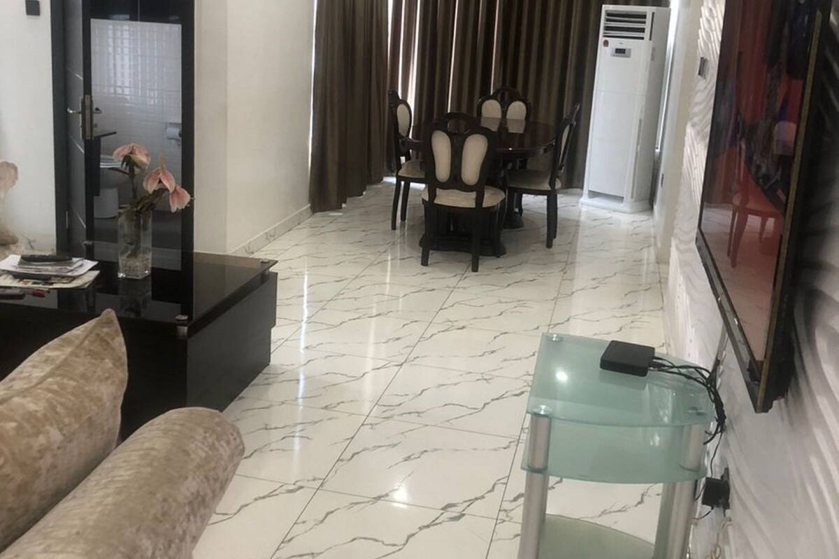 Un salon moderne avec un sol en marbre, une table basse en verre, un canapé, un coin repas avec des chaises, un téléviseur fixé au mur et un appareil de climatisation.