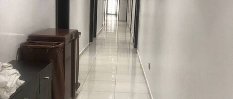 A long, narrow hallway with white walls and a tiled floor, leading to a door at the end.