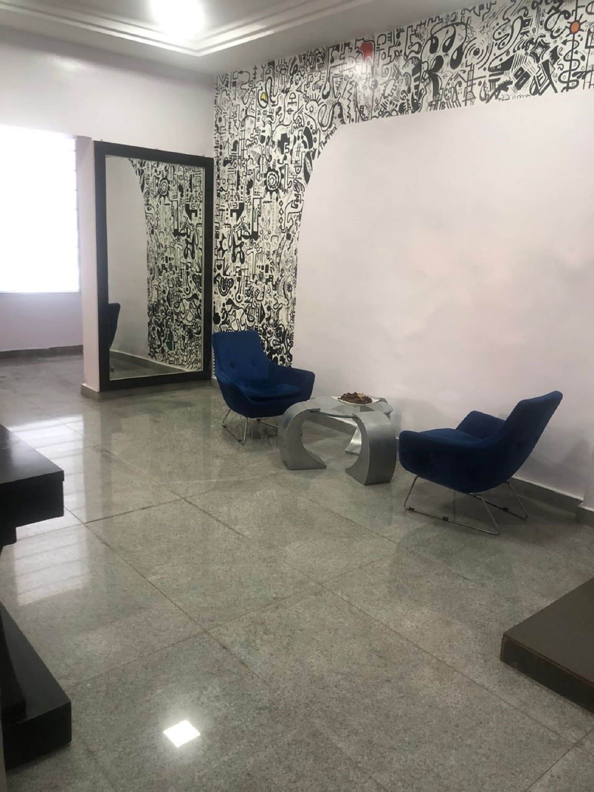 A modern waiting area with two blue chairs, a small table, and a patterned wall.