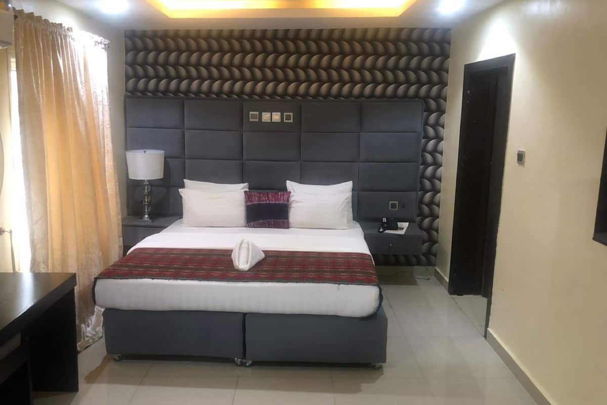Une chambre d’hôtel moderne dotée d’un grand lit, d’une table de chevet, d’une lampe et d’un revêtement mural original au motif texturé.