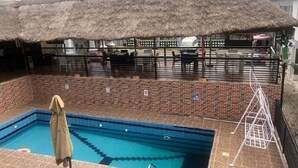 Une piscine avec une terrasse carrelée, une structure à toit de chaume et un mur en briques.
