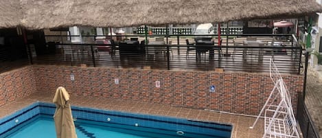 Una piscina con un borde de baldosas, una construcción de techo de paja y un muro de ladrillo.