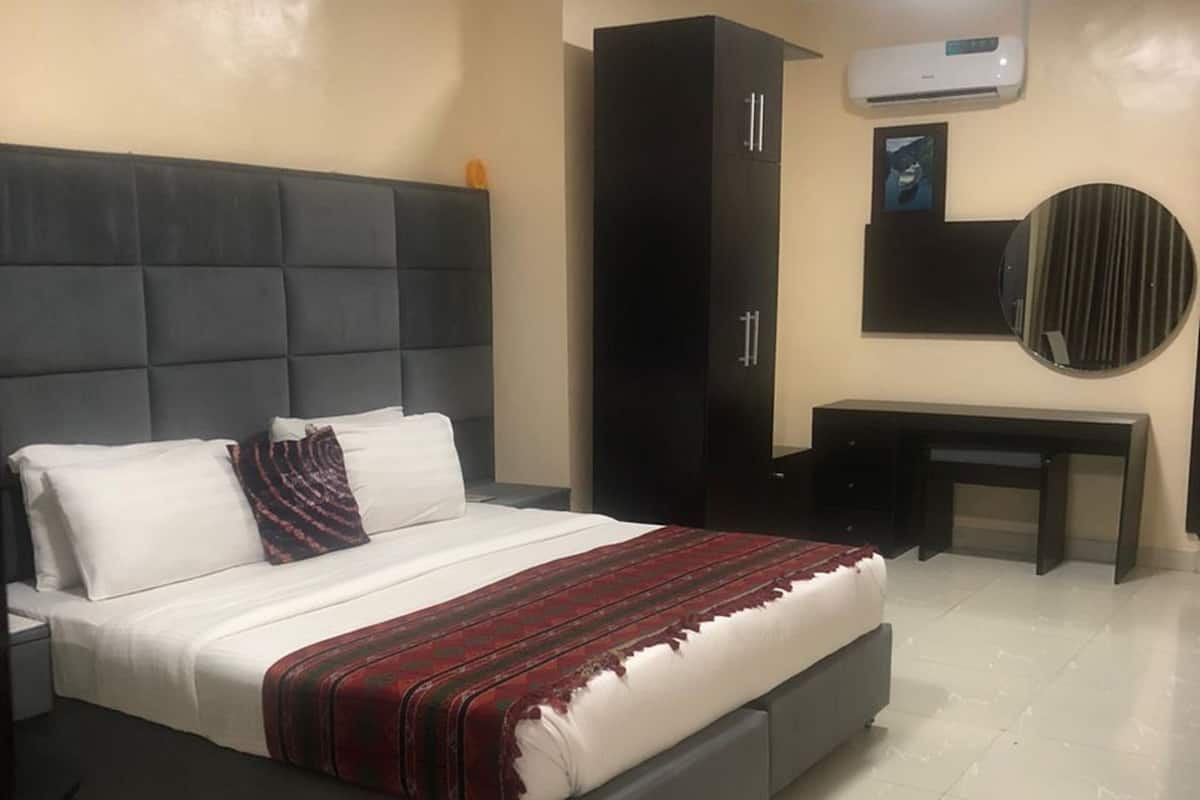 Une chambre moderne avec un grand lit, une tête de lit sombre, une armoire, un bureau et un grand miroir rond accroché au mur.