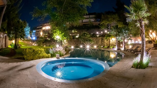 A nighttime swimming pool area with stone flooring, surrounded by trees and illuminated by string lights.