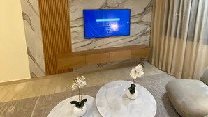 A modern living room with a flat-screen TV mounted on a marble wall, two small marble tables with vases, a sofa, and a wooden panel. - Chez Miguel- Casablanca daily rental with swimming pool (Casablanca)