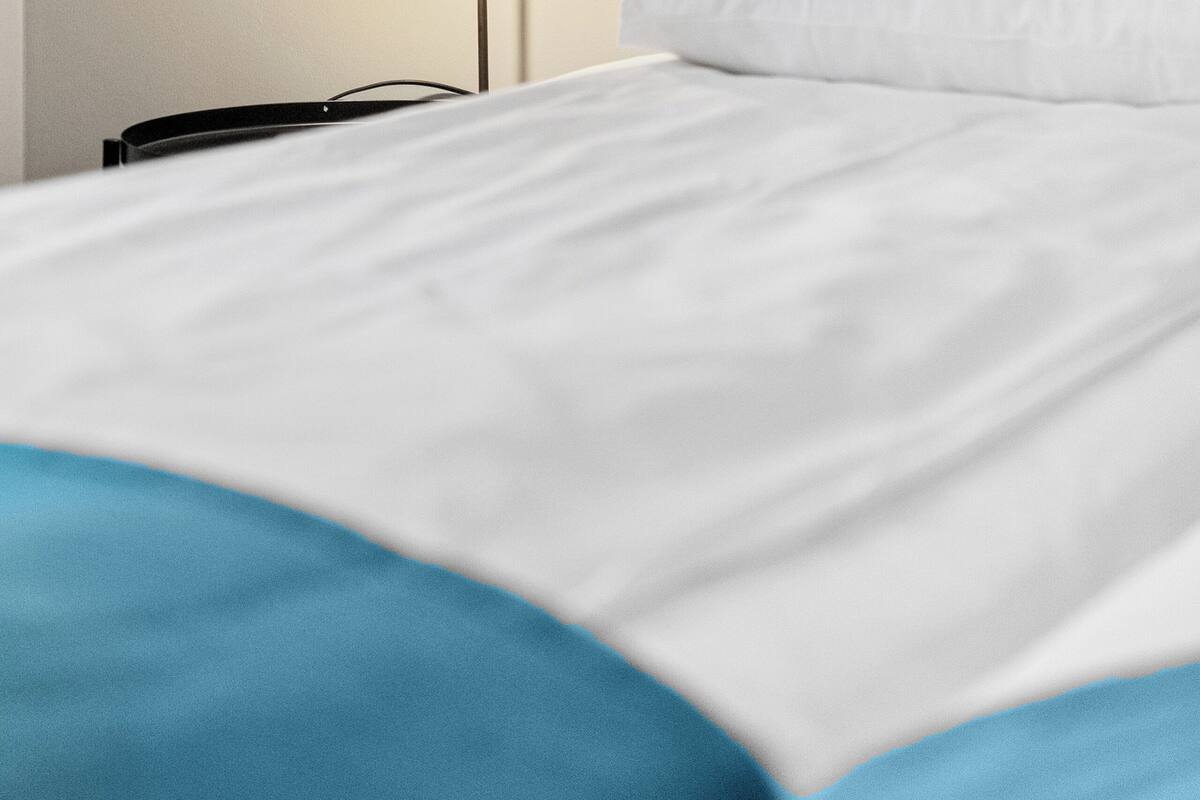 A bed with white and blue bedding, a bedside table, and a wall-mounted light fixture.