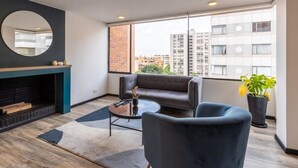 Una sala de estar moderna con chimenea, un sofá, una mesa de centro y vistas de la ciudad a través de amplias ventanas.