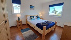 Ein Schlafzimmer mit einem hölzernen Bett, zwei Nachttischen mit Lampen, einem Teppich und einem Fenster mit Blick.
