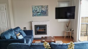 Ein Wohnzimmer mit blauem Sofa, Kamin, Flachbildfernseher und großem Fenster.