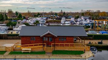 A wooden dock with a small house, a grassy area, and a marina with boats in the background.