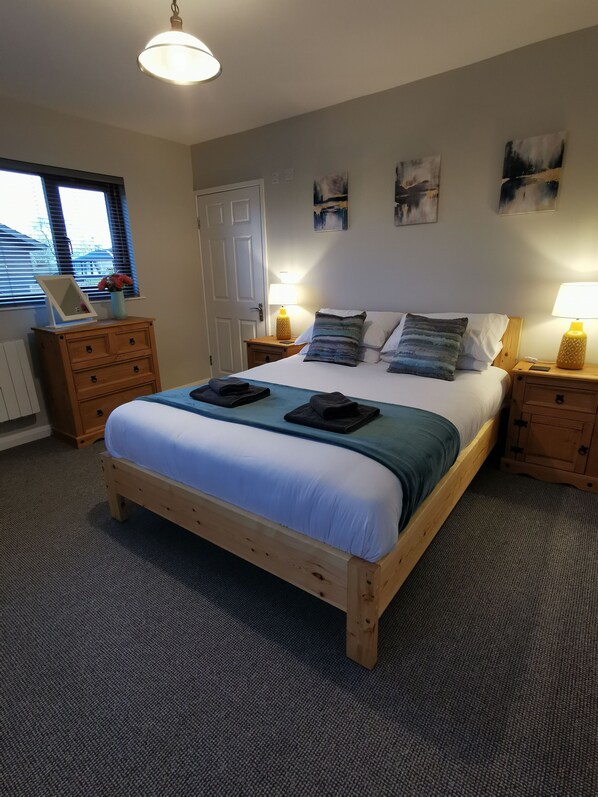 A bedroom with a wooden bed, two bedside tables with lamps, a dresser, and artwork on the walls. - New! River Bay - set on the waters edge - sleeps 4 (Brundall)