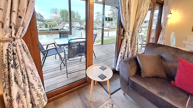 Un salon confortable avec un canapé, une petite table et une vue sur un quai où sont amarrés des bateaux.