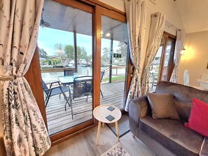 A cozy living area with a sofa, a small table, and a view of a dock with boats. - River Rest  - sleeps 4 guests  in 2 bedrooms (Brundall)