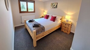 Un lit bien fait, avec des oreillers, une table de chevet avec une lampe, un radiateur et une fenêtre donnant sur un paysage verdoyant.