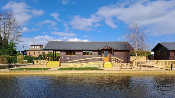 A wooden building with a grey roof, a wooden staircase, and a wooden deck. - River Breeze - Waterside, Norfolk Broads, sleeps 6 in 3 bedrooms (Brundall)