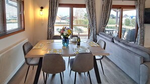 A dining area with a table set for four, a sofa, and a view of the outdoors. - River Breeze - Waterside, Norfolk Broads, sleeps 6 in 3 bedrooms (Brundall)