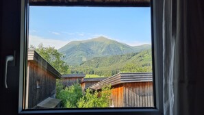 A view through a window of a mountain landscape with wooden buildings. - Cozy vacation home, perfect for families - hiking, skiing on the doorstep (Hohentauern)