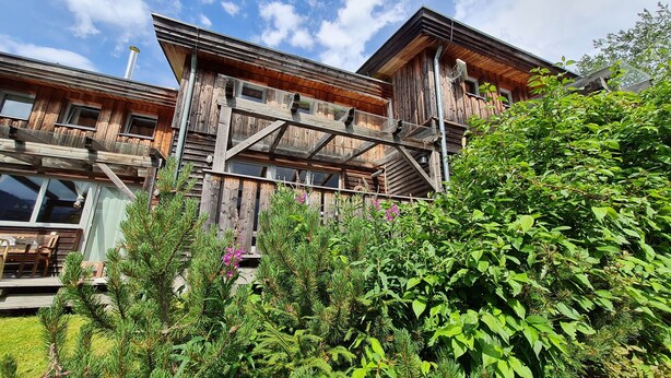 A wooden cabin with a balcony, surrounded by lush greenery and flowering plants. - Cozy vacation home, perfect for families - hiking, skiing on the doorstep (Hohentauern)