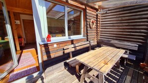 A wooden deck with a wooden table and benches, a window with a red lantern, and a wooden wall with horizontal planks. - Cozy vacation home, perfect for families - hiking, skiing on the doorstep (Hohentauern)
