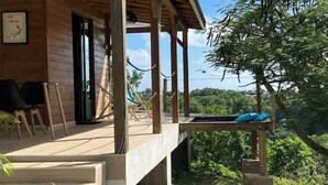 A wooden cabin with a porch, outdoor seating, and a view of the surrounding forest. - Charming bungalow & private pool (Le Gosier, Guadeloupe)