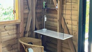 A wooden cabin interior with a sloped ceiling, a wicker chair, a small table, and a door. - Charming bungalow & private pool (Le Gosier, Guadeloupe)