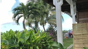 A covered outdoor area with a wooden structure, lush green plants, and a palm tree. - Charming bungalow & private pool (Le Gosier, Guadeloupe)