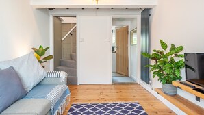 A modern living room with a sofa, a patterned rug, a TV on a wooden stand, and a potted plant. - The Hay Loft - Pass the Keys (Canterbury)