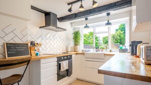 A modern kitchen with white cabinetry, a wooden countertop, a chalkboard sign, and a view of greenery outside. - The Hay Loft - Pass the Keys (Canterbury)
