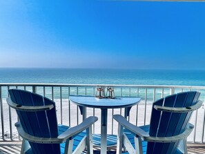 Een balkon met twee blauwe stoelen en een kleine tafel, met uitzicht op een heldere blauwe oceaan.