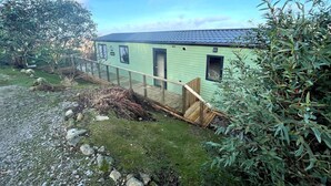 A green house with a blue roof, a wooden deck, and a fenced area. - Beautiful 2BR In Kippford With Incredible Views - Pass the Keys (Dalbeattie)