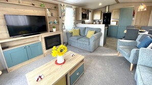 A modern living room with a flat-screen TV, a grey sofa, a wooden coffee table with a vase of flowers, and a kitchen in the background. - Beautiful 2BR In Kippford With Incredible Views - Pass the Keys (Dalbeattie)