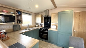 A compact kitchen with a microwave, stove, sink, and wooden cabinets. - Beautiful 2BR In Kippford With Incredible Views - Pass the Keys (Dalbeattie)